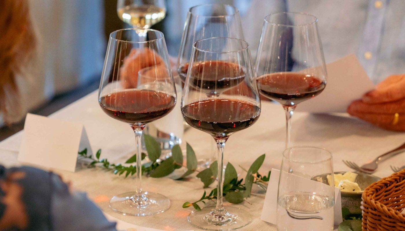 Several glasses of red wine sit on a white table among small plates, herbs, and tasting items.