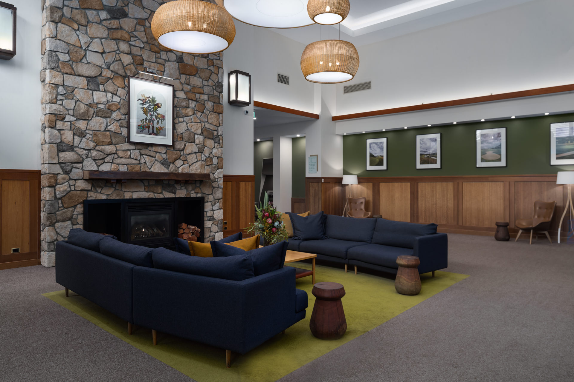 Lounge with dark blue sofas around a stone fireplace, beneath pendant lights and framed wall art.