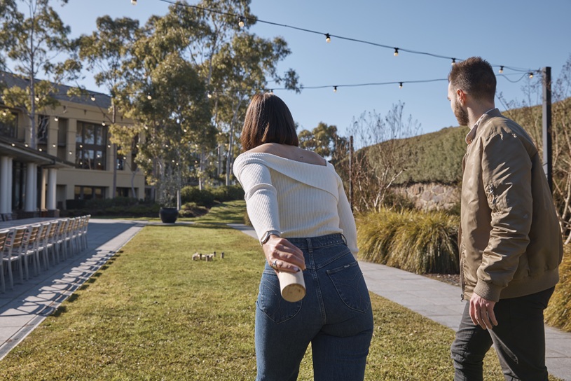 A woman and man stand on a sunny lawn beside a modern building, looking across the grounds.